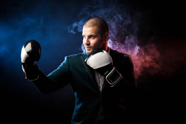 Handsome man sportsman in white shirt, green jacket, black and white boxing gloves boxing and ready to tackle any opposite of red and blue smoke from a wipe on a black isolated background...