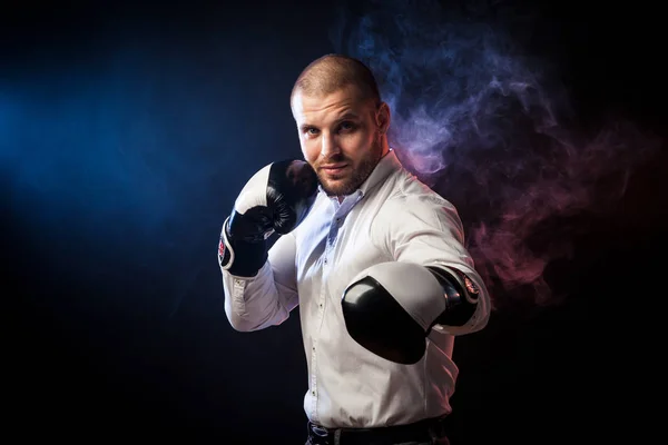 Handsome young man businessman in white shirt and black and white boxing gloves boxing in front of red and blue smoke from a wipe on a black isolated background