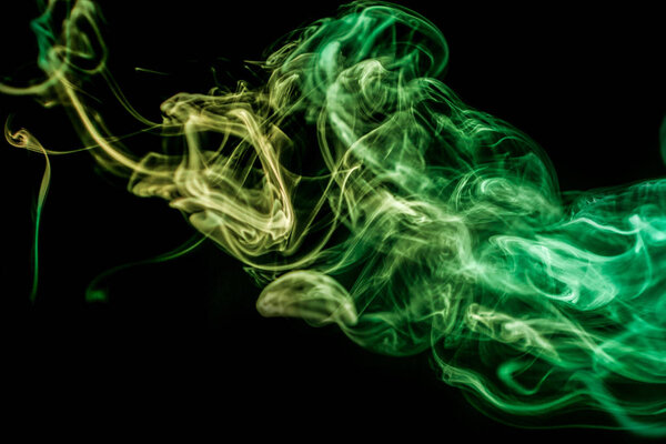 Thick colorful smoke of green on a black isolated background. Background from the smoke of vape