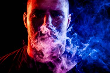 Genç bir adam izole bir siyah mavi ve kırmızı renk renkli duman bulutu exhales. Genç bir hırsız örneği içinde sigara içmek için zarar