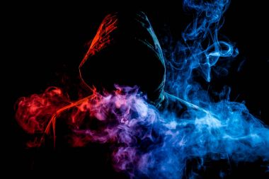 Siyah başlıklı bir genç adam bir vape dumanlar ve exhales renkli mavi, pembe, sarı siyah bir izole arka plan üzerinde duman