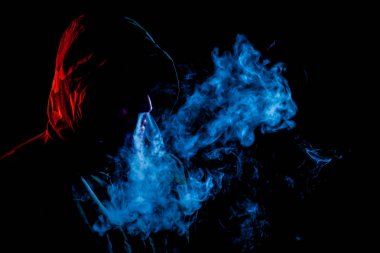 Siyah başlıklı bir genç adam bir vape içiyor ve bir kırmızı, mavi siyah bir izole arka plan üzerinde duman exhales