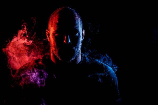 Portrait a young man posing on  colorful  red and blue smoke on a black isolated background