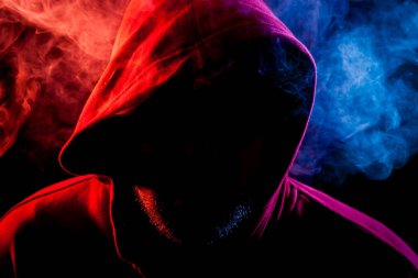 Kırmızı, mavi siyah bir izole arka plan üzerinde duman çevresinde poz bir siyah başlıklı genç bir adam