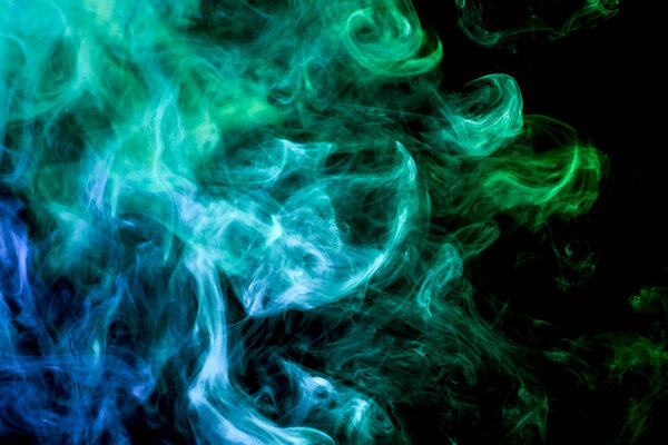 Dense multicolored smoke of blue, and green colors on a black isolated background. Background of smoke vape