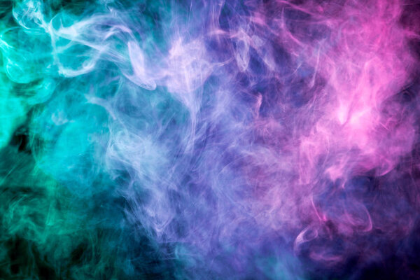 Dense multicolored smoke of blue, pink and green colors on a black isolated background. Background of smoke vape