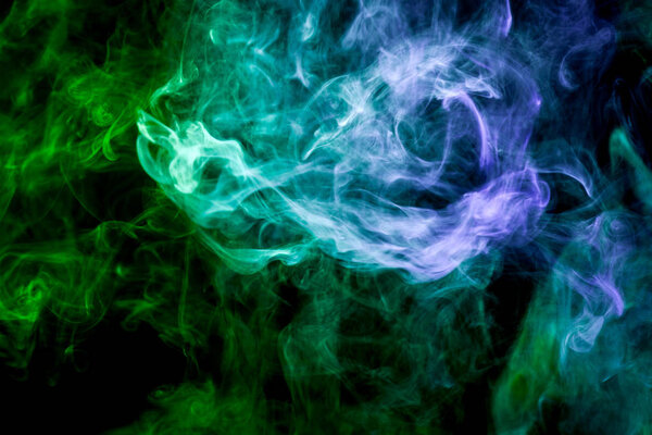 Thick colorful smoke of yellow, green and blue on a black isolated background. Background from the smoke of vape