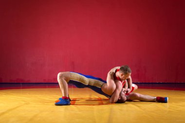 Two greco-roman  wrestlers in red and blue uniform wrestling   on a yellow wrestling carpet in the gym clipart