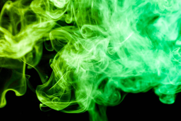 Thick colorful green smoke of blue, pink and purple on a black isolated background. Background from the smoke of vape