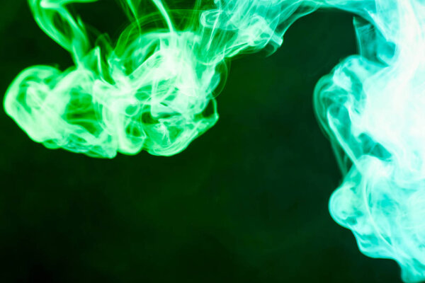 Thick colorful green smoke on a black isolated background. Background from the smoke of vape