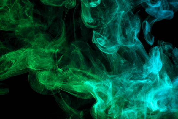 Thick colorful smoke of green and blue on a black isolated background. Background from the smoke of vape