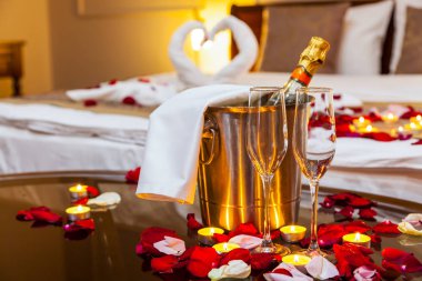 Otel odasında bir balayı için: bir meyve tabağı ve mumlar, arka planda bir yatak havlu kuğular ile dekore edilmiş ve gül yaprakları içeren bir tablo