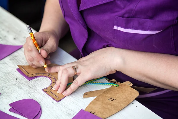テーブルの上の本革子供靴を紫の制服でお針子として働いている若い女性のクローズ アップ カットします — ストック写真