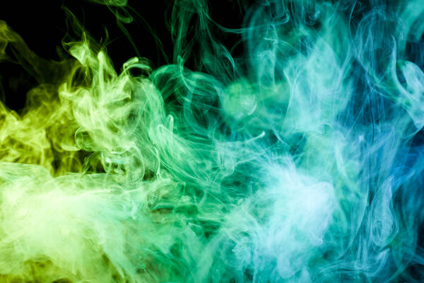 Thick colorful green, yellow and blue smoke on a black isolated background. Background from the smoke of vape