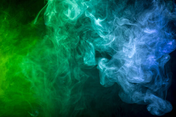 Colorful green, blue and yellow smoke on a black isolated background. Background from the smoke of vape