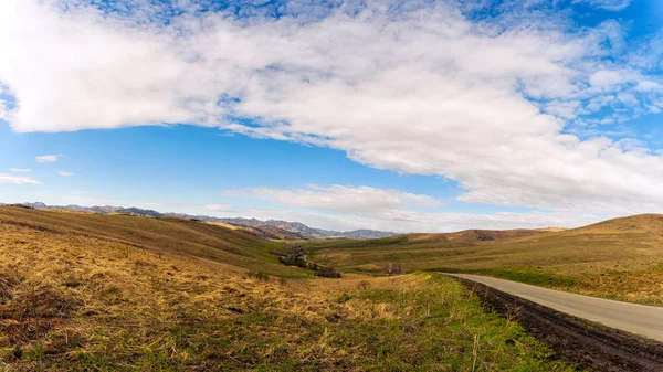 stock image Landscape of the high mountains of the Altai of the Chemal district in early spring with coniferous and birch forests and the road, the sky is covered with clouds