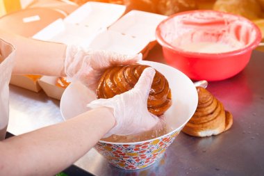 Koruyucu eldiven Bayan baker bir close-up buns cinnabon hazırlar ve krem onları fırında dökülen