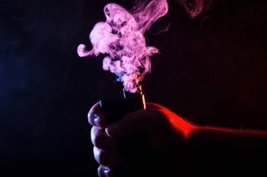 Close-Up bir vape sigara içiyor elinde tutan bir adam. Renkli duman Sigara