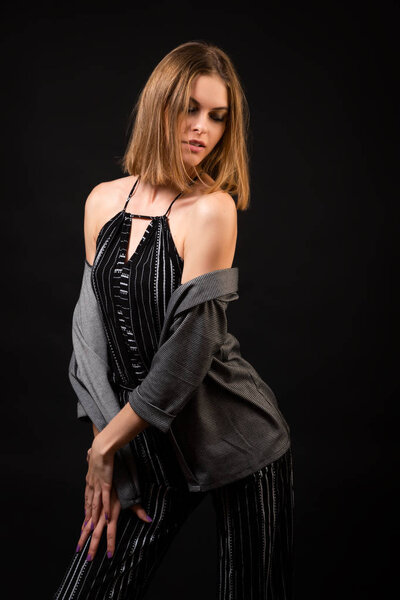 Young beautiful woman wearing in black overalls and cardigan  posing over black background, top view. Studio shot of  brunette woman against isolated background