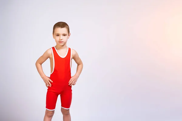 赤いレスリングのタイツ姿の明るい少年の肖像画は 彼の側に彼の手を保持し 自信を持ってカメラを見て 白い孤立した背景にポーズをとります 小さな戦闘機の選手の概念 — ストック写真