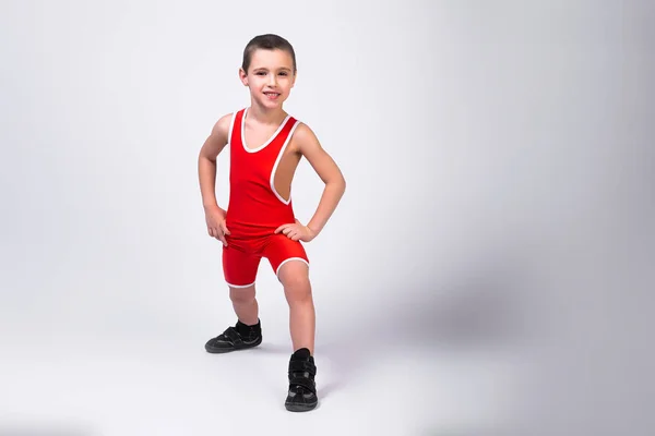 赤いスポーツのOrtsovskoyのLeotard及びレスリングのブーツの小さい面白い男の子は白い隔離された背景の彼の達成で練習そして微笑をすることを楽しみにしていた 小さな戦闘機の選手の概念 — ストック写真