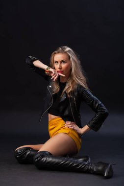 Çekici kaltak kadın. Sarı etekli şık elbiseli güzel bir kadın, siyah deri ceketli ve stüdyo çekiminde poz veren çekici bir sürtük. Modern başarılı bir kadının portresi.