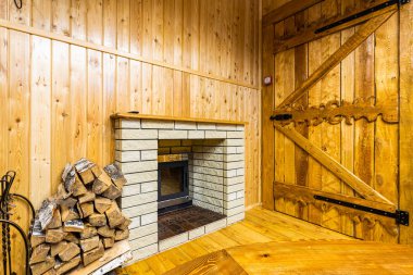 Kayadan yapılmış büyük bir şömineyi söndürün, hemen yanında ateş yakmak için hazırlanmış kuru kütükler var, duvar ve zemin el çırpma tahtasıyla süslenmiş, kapı güzel bir şekilde platform bandıyla süslenmiş. 