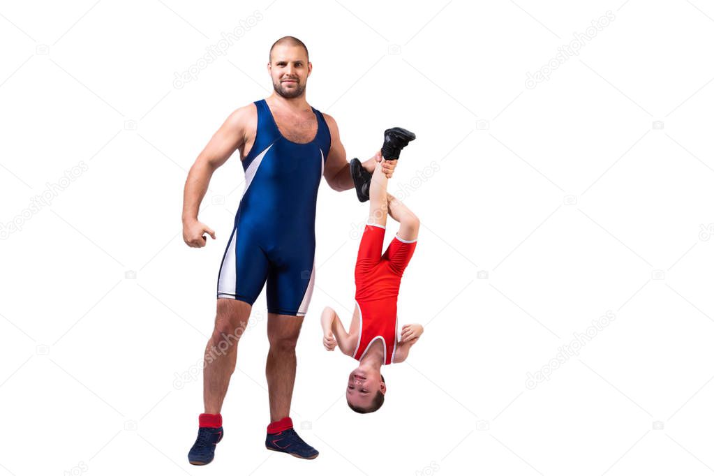 Men in wrestling tights and wrestlers holds the foot of a wrestler boy on a white isolated background. Dad and son have been fooling around forever.Teaching children Greco-Roman wrestling