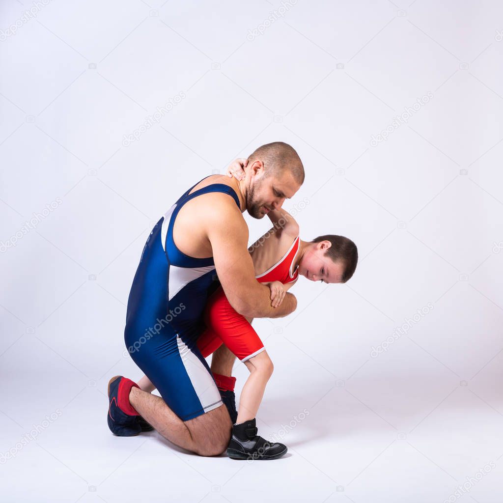 A  wrestler boy in a sports tights wrestles with an adult male wrestler on a white isolated background. The concept of child power and martial arts training. Teaching children Greco-Roman wrestling