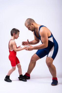 Spor tayt giymiş bir güreşçi çocuk beyaz tenli bir arka planda yetişkin bir erkek güreşçiyle güreşiyor. Çocuk gücü ve dövüş sanatları eğitimi kavramı. Çocuklara Greko-Romen güreşi öğretmek