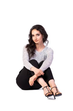 Güzel bluzlu, parlak makyajlı çekici bir kadın parıltılı, siyah pantolonlu ve sandaletli bir kadın gülümsüyor ve izole edilmiş beyaz bir arka planda yere oturuyor. Fotoğraf stüdyosunda poz veren bir kadın.