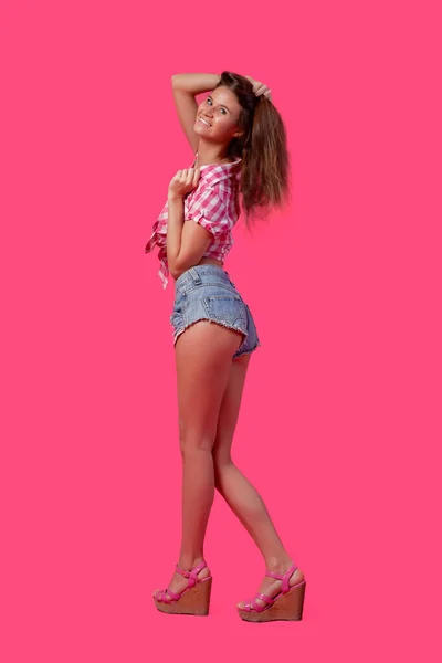 夏天的照片上 一个兴奋的年轻微笑的女人穿着粉色泳衣 格子衬衫和斜纹棉布短裤摆姿势 并在粉色孤立的背景下享受乐趣 粉红快乐的心情 — 图库照片