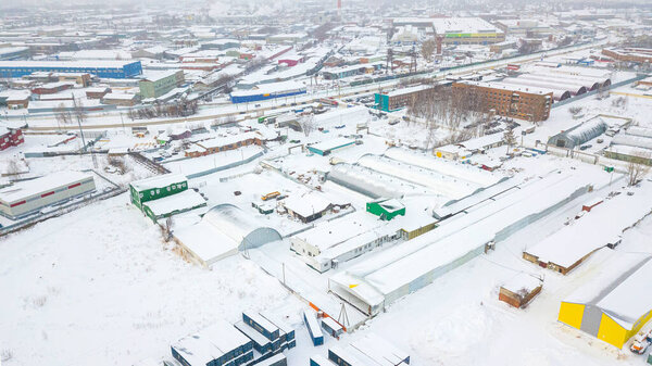 Top view of the industrial zone: railway rails, garages, warehouses, containers for storing goods in snow day. The concept of storage of goods by importers, exporters, wholesalers, transport enterprises, customs