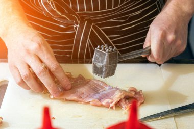 Siyah önlüklü yakın plan erkek şef profesyonel bir mutfakta metal çekiçle tavuk eti yiyor.