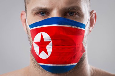 Kuzey Kore bayrağının renklerine boyanmış tıbbi maskeli, yaralı gözlü genç bir adam.