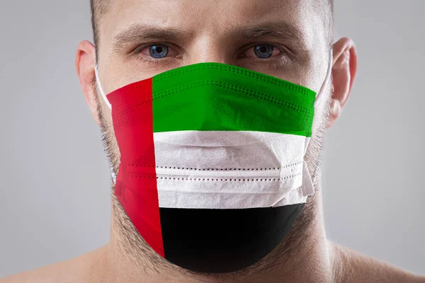 Young man with sore eyes in a medical mask painted in the colors of the national flag of United Arab Emirates. Medical protection against airborne diseases, coronavirus. Man is afraid of getting the flu