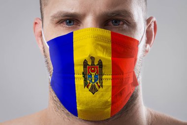 Tıbbi maske takmış, Moldova bayrağının renklerine boyanmış yaralı gözleri olan genç bir adam. Hava hastalıklarına karşı tıbbi koruma, koronavirüs. Adam grip olmaktan korkuyor.