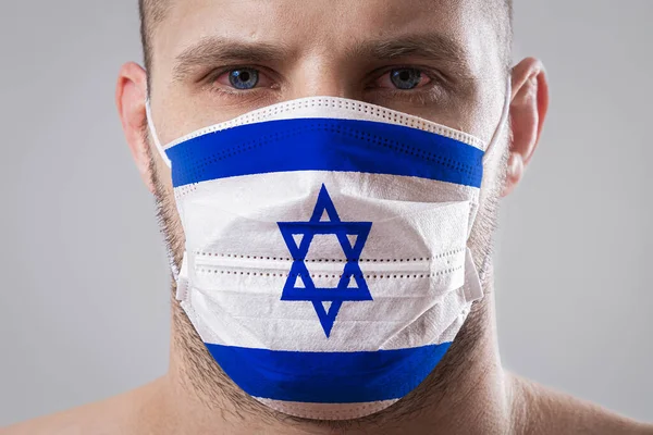 Young man with sore eyes in a medical mask painted in the colors of the national flag of Israel. Medical protection against airborne diseases, coronavirus. Man is afraid of getting the flu