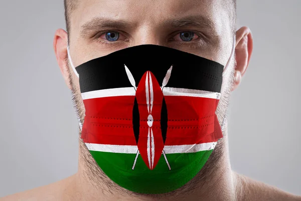 Young man with sore eyes in a medical mask painted in the colors of the national flag of Kenya. Medical protection against airborne diseases, coronavirus. Man is afraid of getting the flu