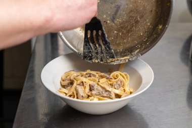 Yakın plan erkek şef, büyük kral karidesleri ve krema soslu makarnayı kızartma tavasından tabağa karıştırıyor. Karides makarna yapma süreci