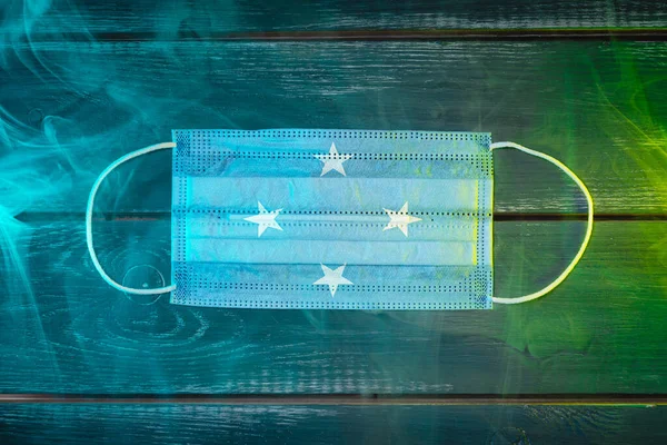 Medical mask for protection against airborne diseases, painted in the national flag of Federal States of Micronesia on a black background in blue-green smoke. Medical protection against airborne diseases, coronavirus