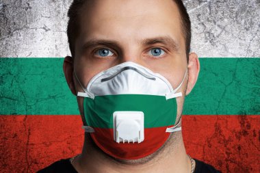 Bulgaristan bayrağının renklerine boyanmış tıbbi maskeli, yaralı gözlü genç bir adam. Coronovirus hastalığı COVID-19 konsepti. Adam grip olmaktan korkuyor.