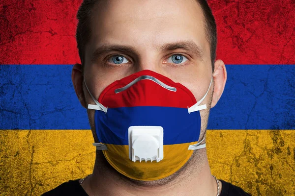 Young man with sore eyes in a medical mask painted in the colors of the national flag of Armenia. Coronovirus disease  COVID-19 concept.  Man is afraid of getting the flu