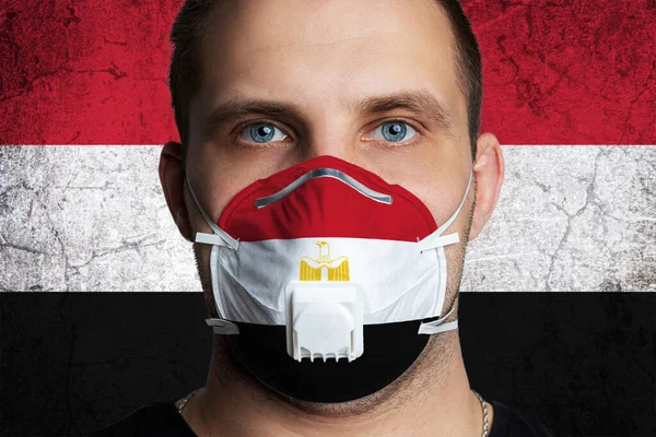 Young man with sore eyes in a medical mask painted in the colors of the national flag of Egypt. Coronovirus disease  COVID-19 concept.  Man is afraid of getting the flu