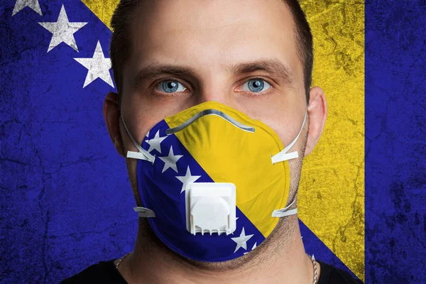 Young man with sore eyes in a medical mask painted in the colors of the national flag of Barbados. Coronovirus disease  COVID-19 concept.  Man is afraid of getting the flu