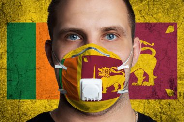 Sri Lanka bayrağının renklerine boyanmış tıbbi maskeli, yaralı gözlü genç bir adam. Coronovirus hastalığı COVID-19 konsepti. Adam grip olmaktan korkuyor.