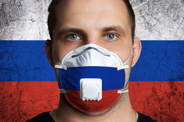Young man with sore eyes in a medical mask painted in the colors of the national flag of Russia. Coronovirus disease  COVID-19 concept.  Man is afraid of getting the flu