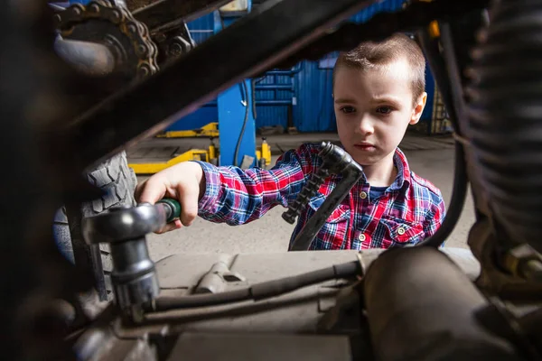 少年は大人になって車を修理することを夢見ている 若い自動車労働者の少年は サービスステーションのガレージでレンチでナットを外します — ストック写真