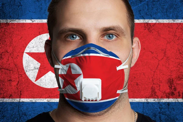 Young man with sore eyes in a medical mask painted in the colors of the national flag of North Korea. Coronovirus disease  COVID-19 concept.  Man is afraid of getting the flu