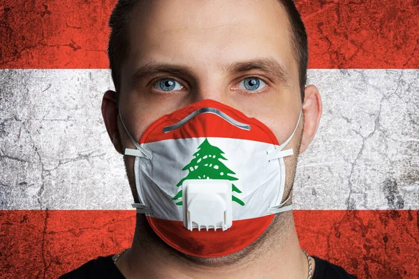 Young man with sore eyes in a medical mask painted in the colors of the national flag of Lebanon. Coronovirus disease  COVID-19 concept.  Man is afraid of getting the flu